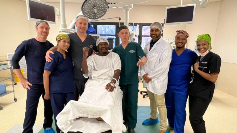 The full surgical team gathered around a patient after a successful procedure.